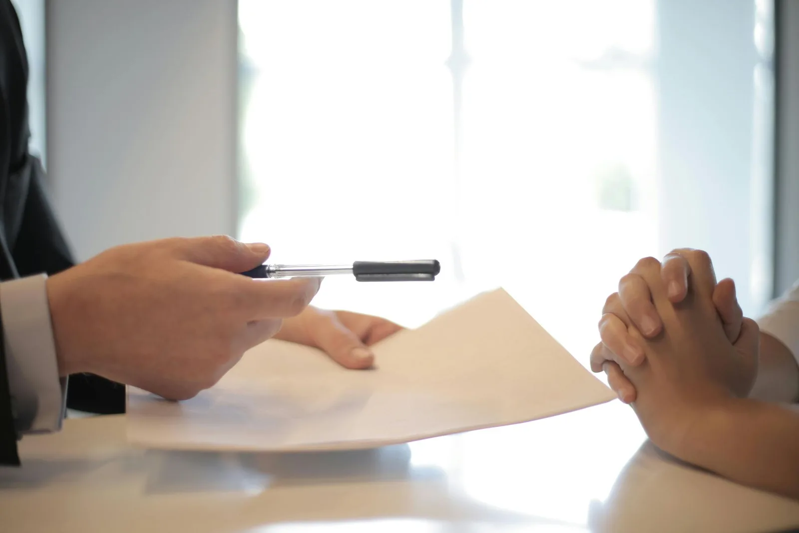 Life Insurance An agent passing a pen across a desk to a client about to sign a life insurance policy.