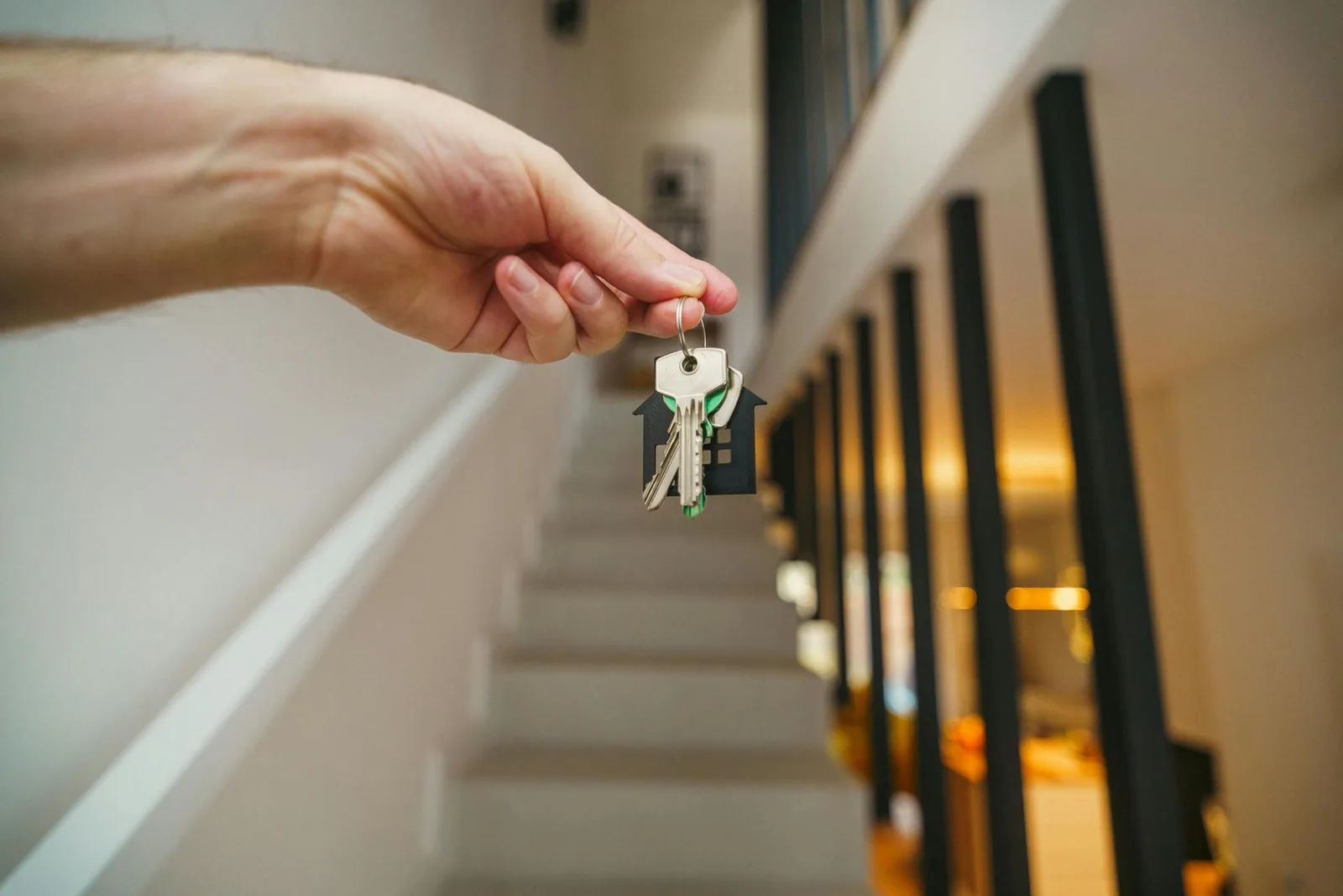 Hand holding house keys in front of a staircase.