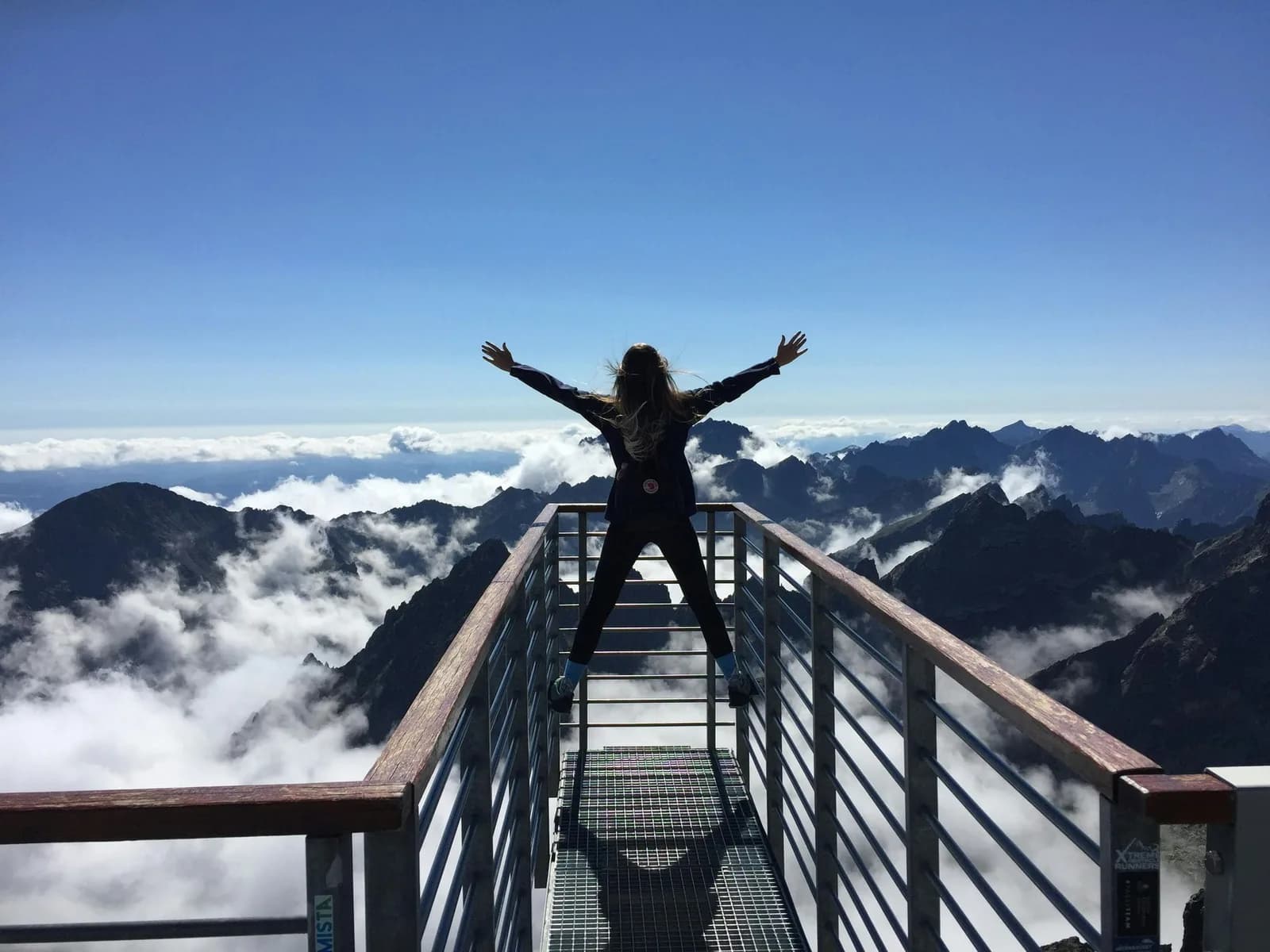 Umbrella Policies Person standing on a mountain overlook with arms raised above a valley of clouds.